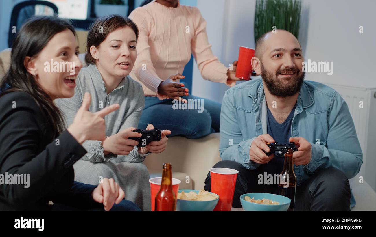 Gros plan de l'homme et de la femme utilisant des contrôleurs pour jouer à des jeux vidéo sur la console tv pour faire une activité amusante après le travail. Collègues qui s'amusant à jouer à la télévision et à boire au bureau après les heures d'ouverture. Banque D'Images