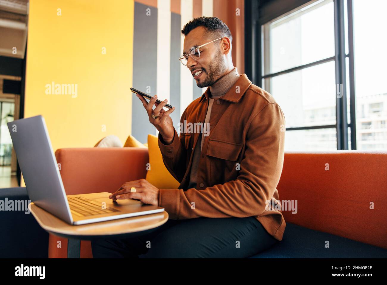 Homme d'affaires souriant parlant au téléphone et utilisant un ordinateur portable dans un espace de travail conjoint. Heureux jeune entrepreneur de faire des plans avec ses associés d'affaires Banque D'Images
