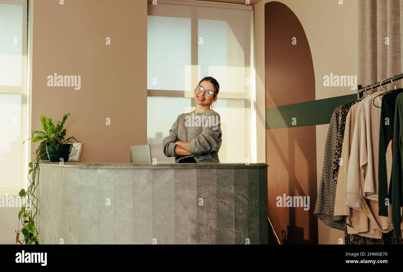 Femme entrepreneur souriant à la caméra tout en se tenant derrière le comptoir dans son magasin de vêtements. Propriétaire d'une petite entreprise prospère travaillant à la Fran Banque D'Images