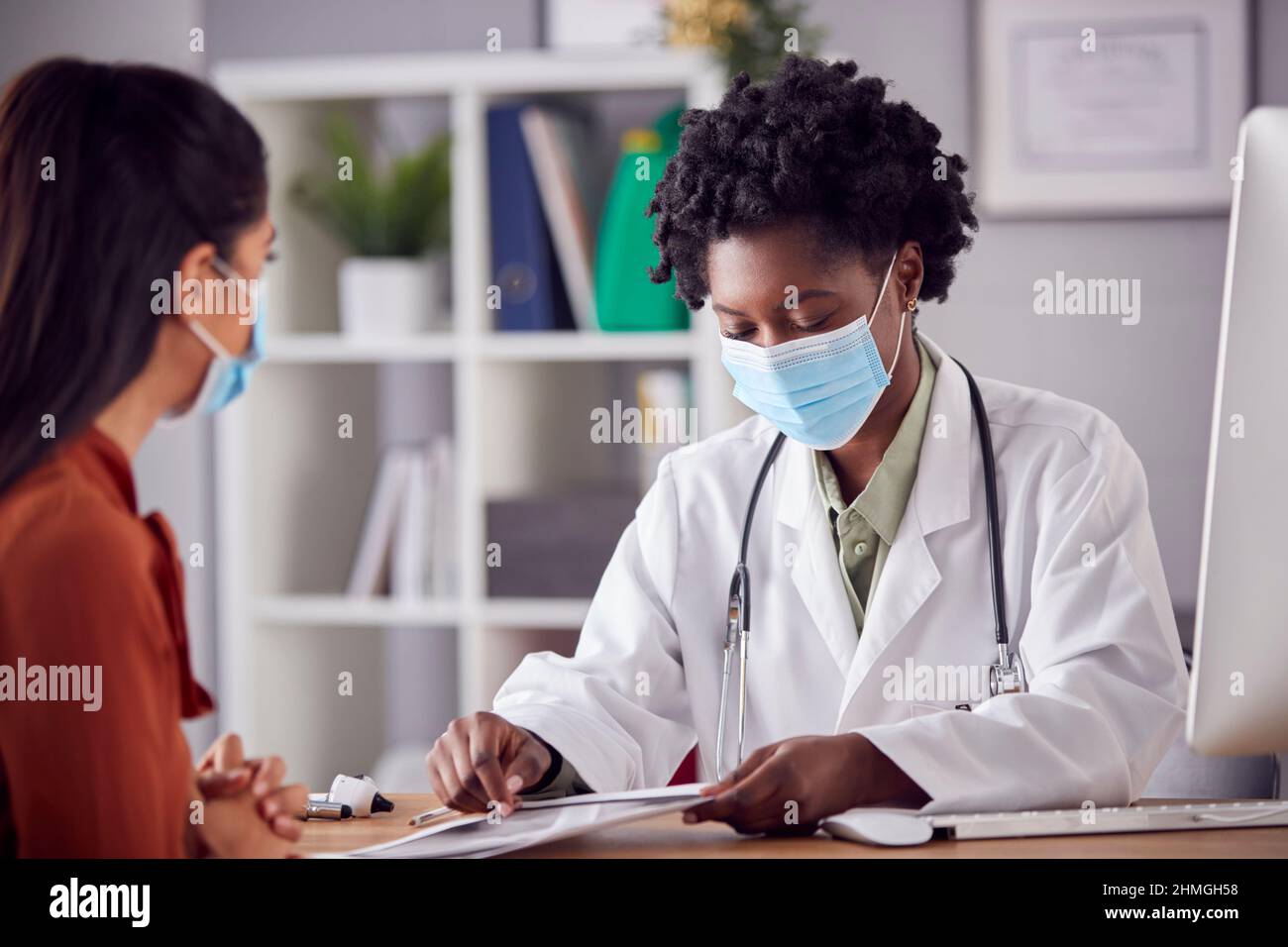 Femme médecin en manteau blanc portant un masque facial ayant une rencontre avec une femme mature patient au bureau Banque D'Images