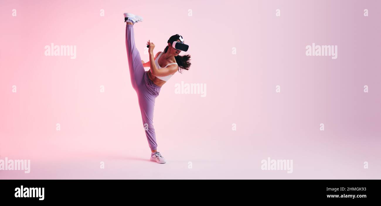 Jeune femme sportive qui s'efforce tout en portant un casque de réalité virtuelle. Jeune femme sportive qui s'étire les jambes lors d'une séance d'entraînement virtuelle. BT Banque D'Images