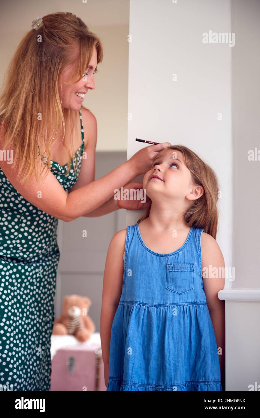 Mère mesurant la taille de la fille et marquant sur le mur à la maison Banque D'Images