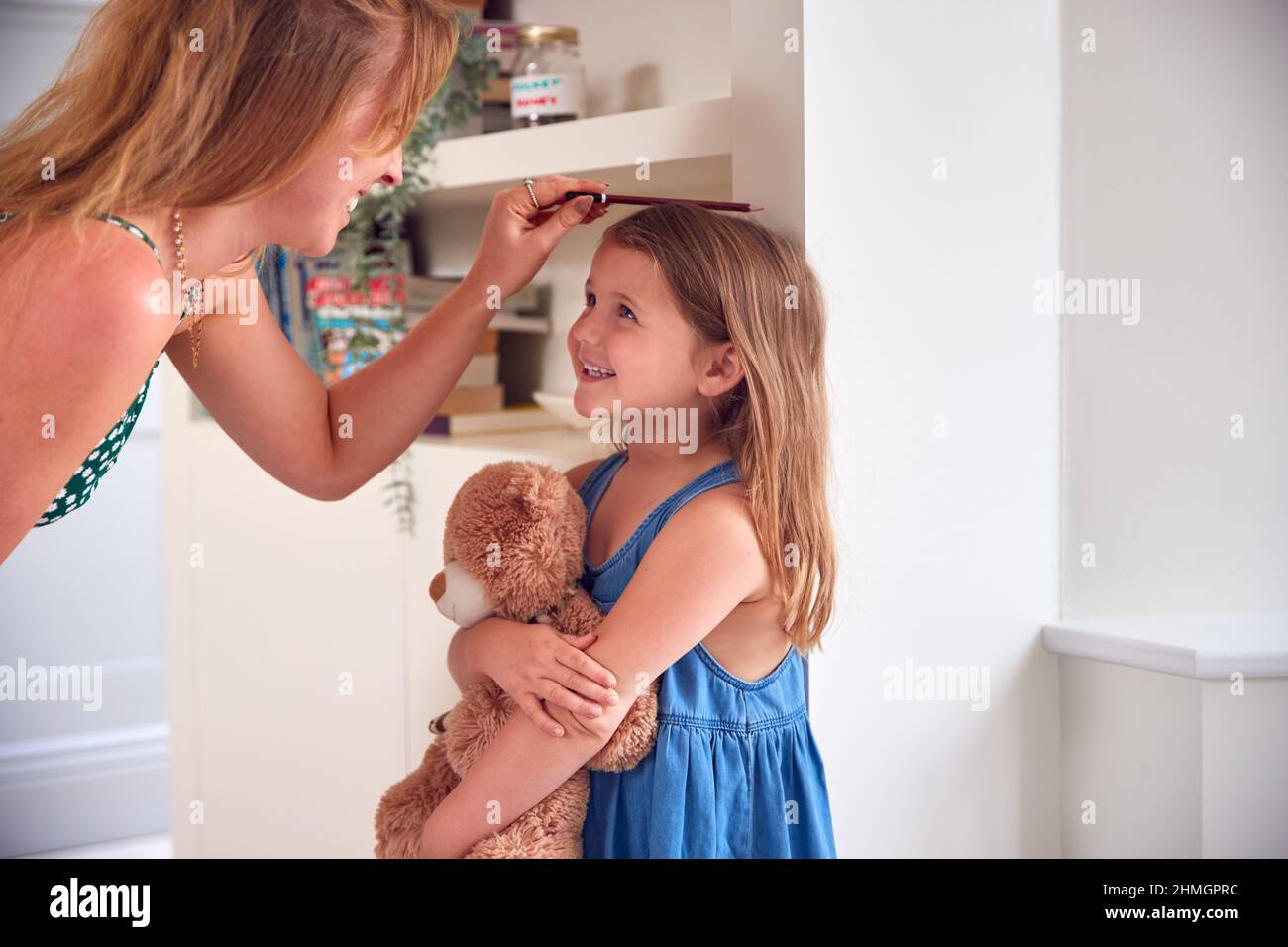 Mère mesurant la taille de la fille et marquant sur le mur à la maison Banque D'Images