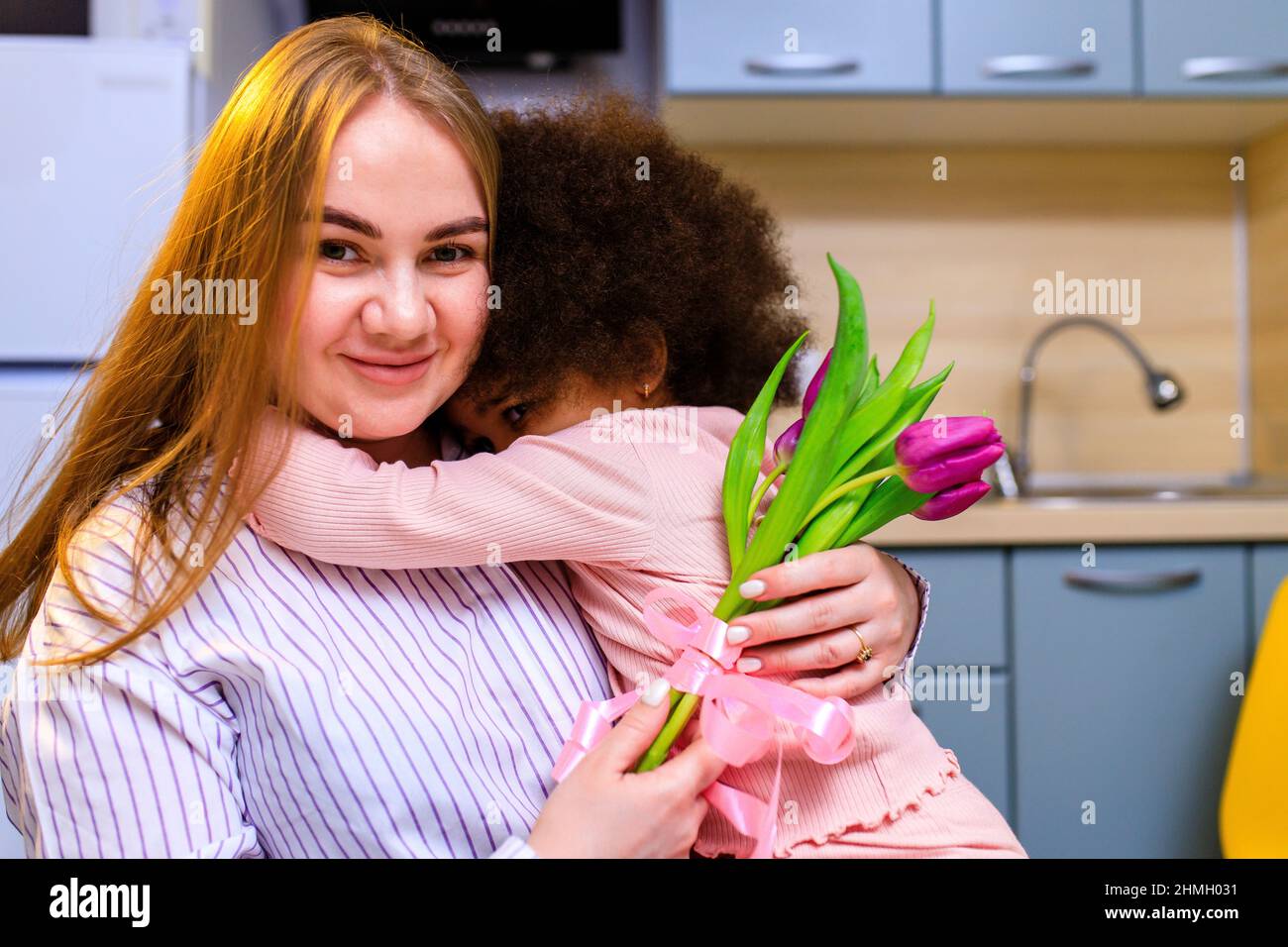 mère polyethnique et sa fille avec une coiffure afro assise dans la cuisine avec un bouquet de tulipes et une carte d'extension Banque D'Images