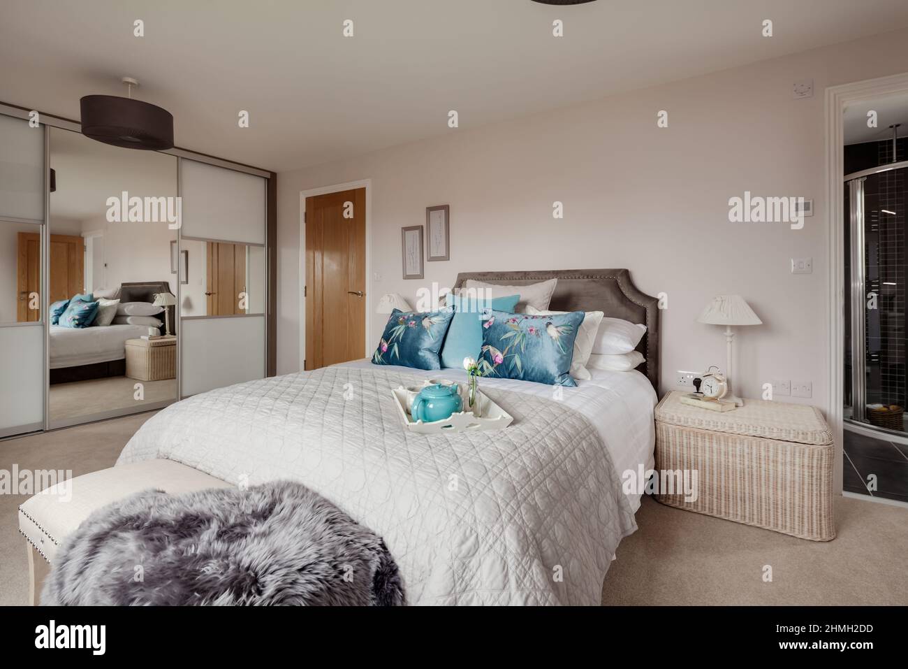 Newport, Essex - Mars 21 2019: Chambre principale moderne de luxe avec armoires à miroirs, porte ouverte à la salle de bains attenante et lit habillé. Banque D'Images