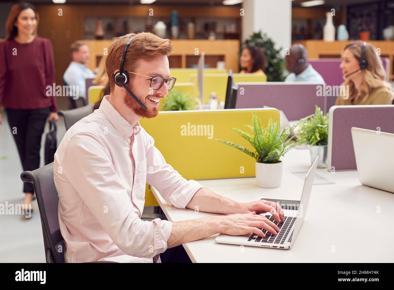 Homme d'affaires portant un casque parlant à l'appelant dans un centre de services à la clientèle très occupé Banque D'Images