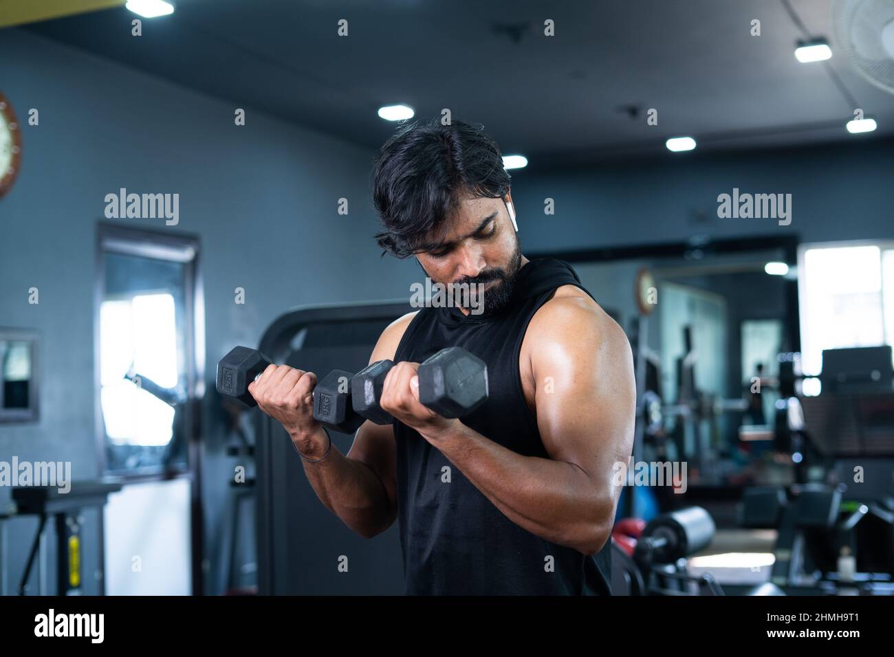 Un jeune homme s'exerce avec des haltères pour les biceps à la salle de gym - concept de musculation, centre de fitness, mode de vie sain, musculation et Banque D'Images