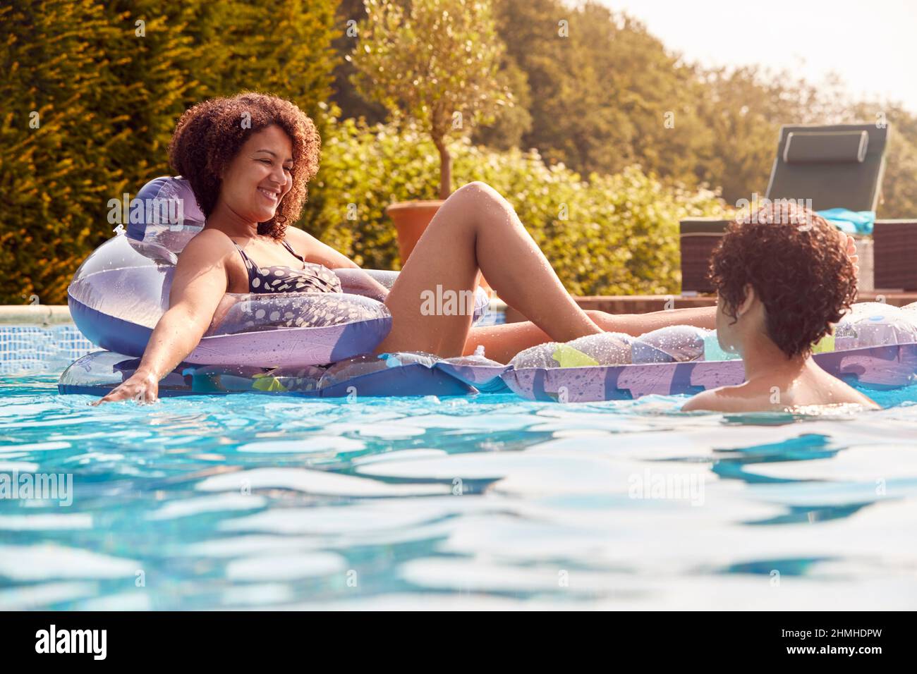 Une femme se détendant flottant dans la piscine tandis qu'un fils adolescent naque à côté d'elle pendant les vacances d'été Banque D'Images