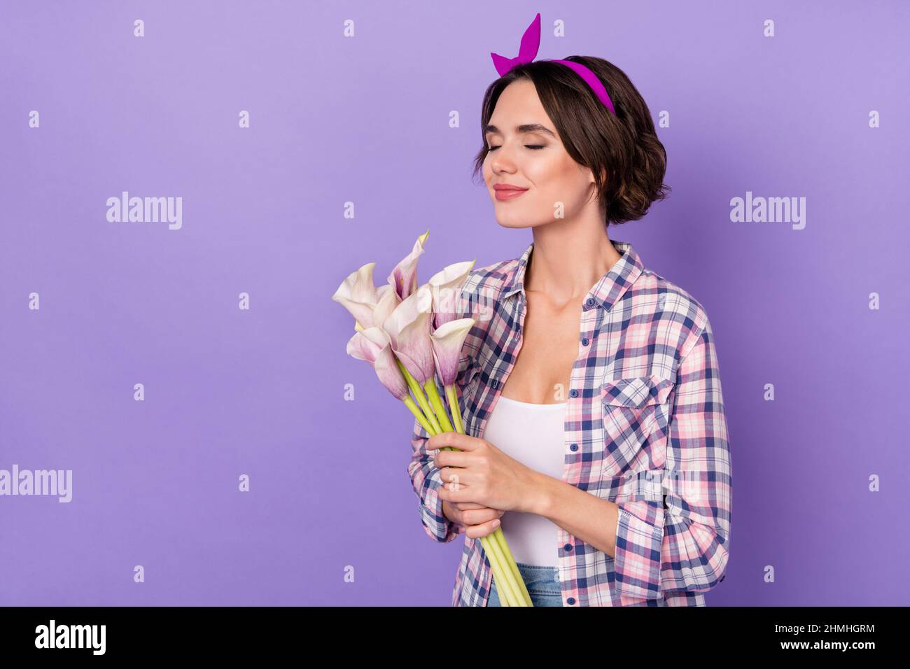 Profil côté photo de la jeune femme charmante profiter de l'odeur des lis 8-mars isolé sur fond violet couleur Banque D'Images