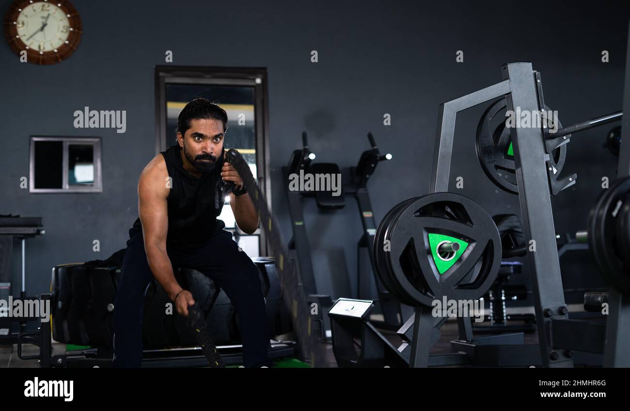 Jeune athlète indien s'exerçant en utilisant des cordes de combat ou lourdes à l'entraînement de gym - concept d'entraînement intensif, gymnastique, détermination et Banque D'Images