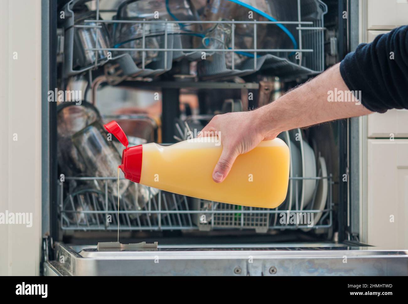 bras d'un homme tenant une bouteille de détergent et la versant dans le lave-vaisselle Banque D'Images