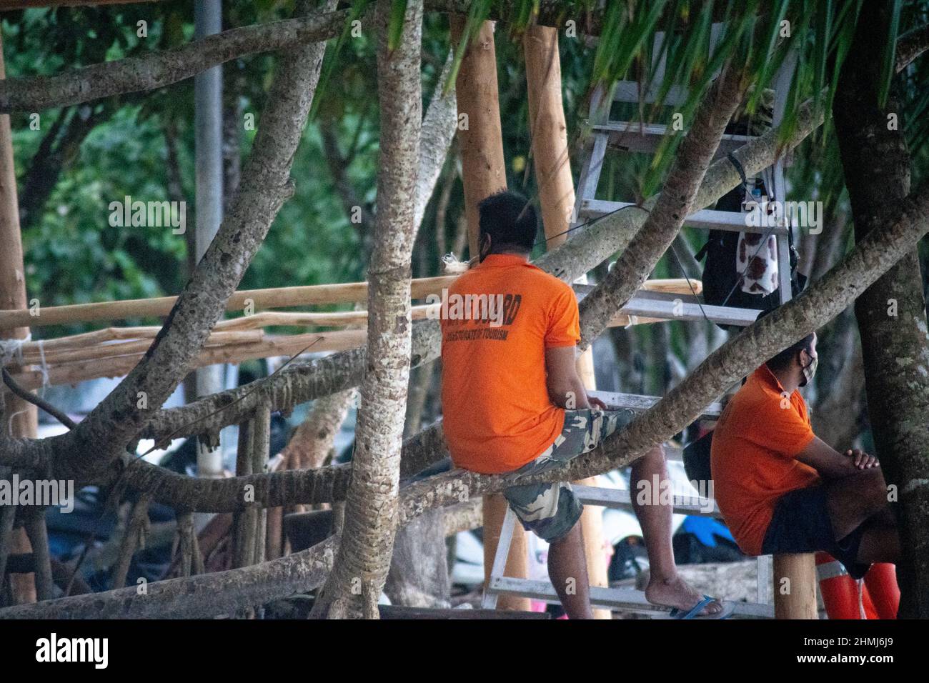 maître nageur en chemise orange assis sur un arbre à la plage avec des touristes en arrière-plan à havelock swaraj dweep andaman nicobar îles inde Banque D'Images