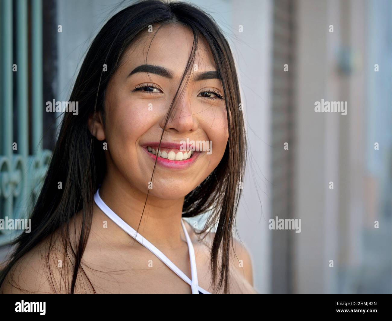 Joyeuse positive belle fille mexicaine à yeux bruns sourit et regarde le spectateur en face d'une maison de la vieille ville avec un grill de fenêtre en fer forgé. Banque D'Images