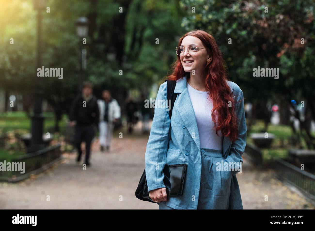 Belle jeune femme d'affaires vêtue d'un costume bleu tenant une tablette numérique à l'extérieur, femme architecte professionnelle marchant au parc, lumière d'éclat Banque D'Images