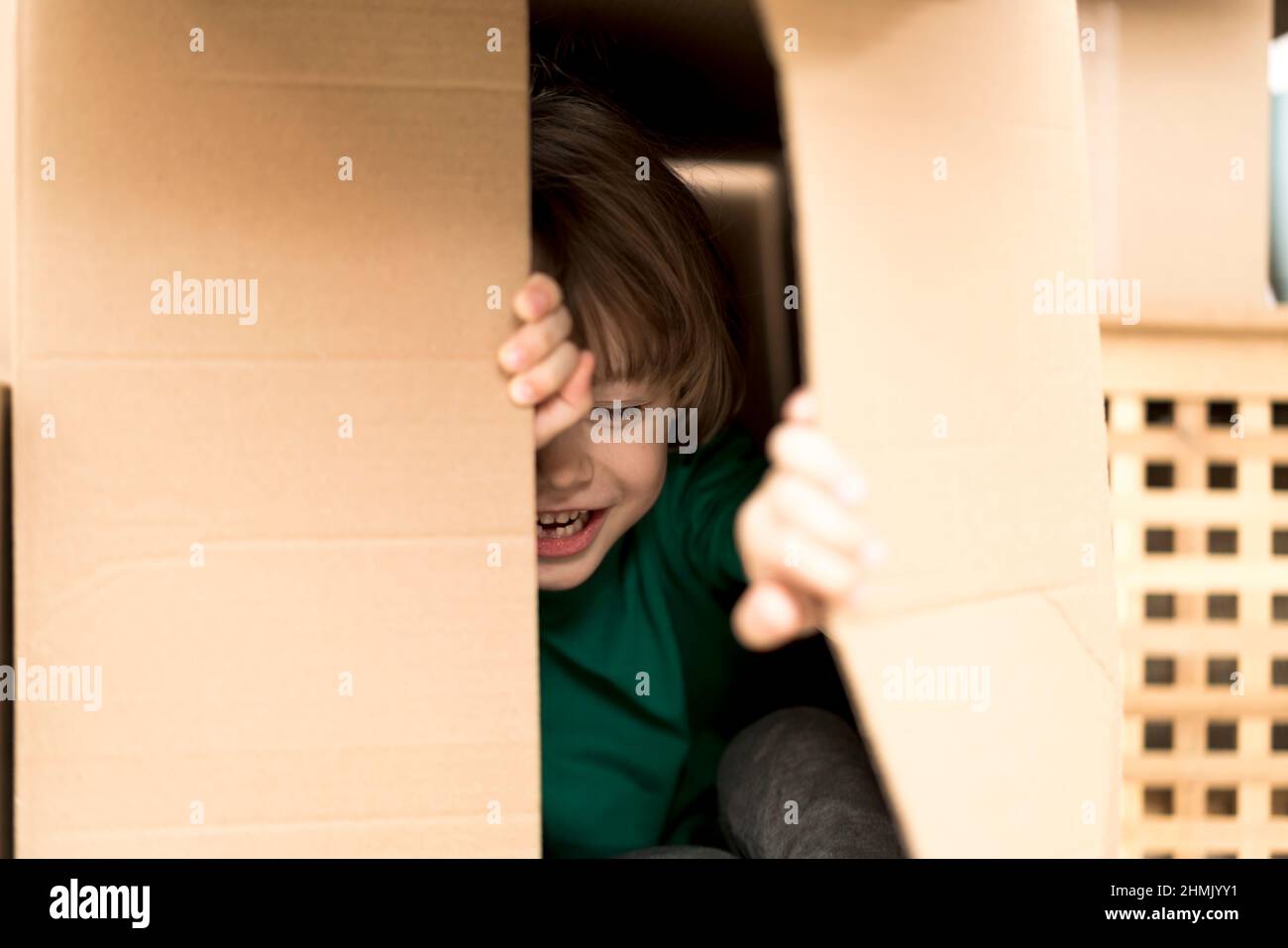 Garçon se cachant dans une énorme boîte en carton. Il joue et joue à travers un trou dans la boîte. Un enfant est heureux de s'installer dans une nouvelle maison. Banque D'Images