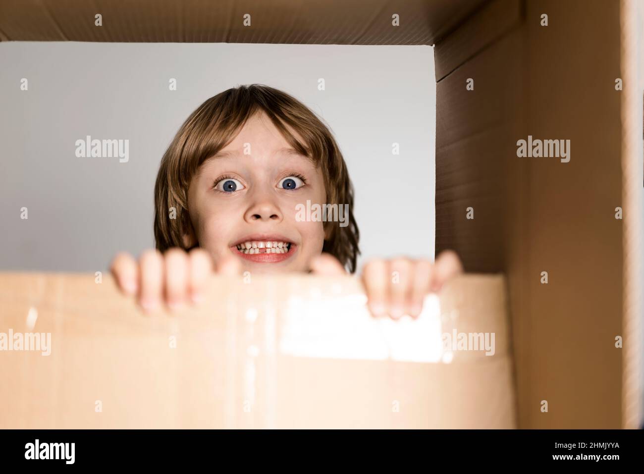 Un petit garçon excité sautant à l'intérieur d'une énorme boîte en carton. Il joue et regarde hors d'une boîte. Un enfant est heureux de s'installer dans une nouvelle maison. Banque D'Images