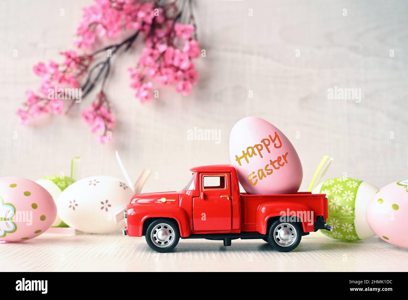 Un œuf de Pâques sur une petite voiture sur un fond clair et une branche en fleurs. Copier l'espace. Carte de Pâques. Banque D'Images