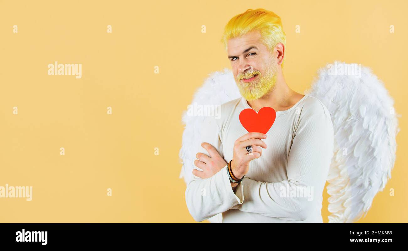 Cupidon à coeur rouge. Bel ange avec ailes blanches. Concept d'amour. Saint-Valentin. Homme barbu. Banque D'Images