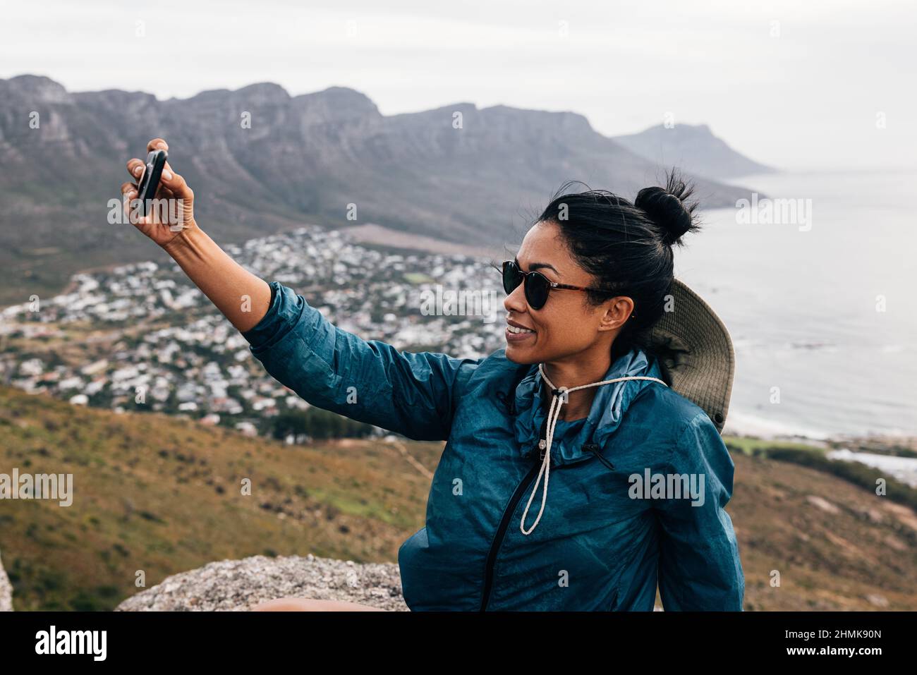 Jeune femme en lunettes de soleil, tenant un smartphone et prenant un selfie tout en faisant une pause pendant une randonnée en montagne Banque D'Images