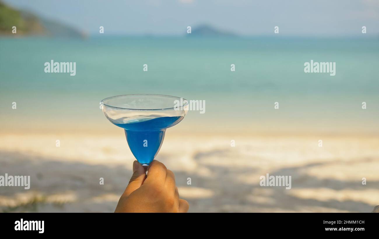 Homme mains secouer les cocktails bleus dans des verres de vin se reposant sur la plage dans l'ombre près de calme azure océan vue proche. Voyager dans les pays tropicaux. Gros plan. Banque D'Images