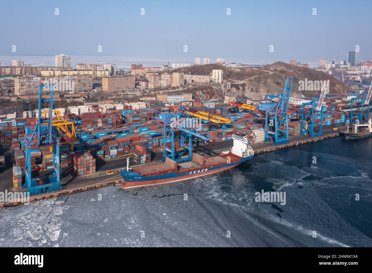 Vladivostok, Russie - 27 janvier 2022 : Vue de dessus du terminal des conteneurs du port maritime et de la ville.En hiver, un bateau à conteneurs est en train de charger au quai. Banque D'Images