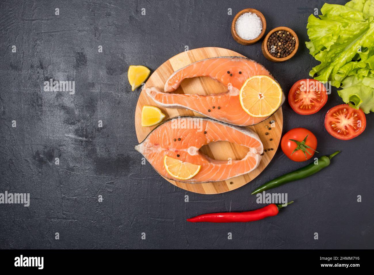 deux steaks de saumon cru sur un plan de cuisine rond avec des ingrédients pour la cuisson. source d'oméga 3 et de gras saturés. vue du dessus. fond noir Banque D'Images