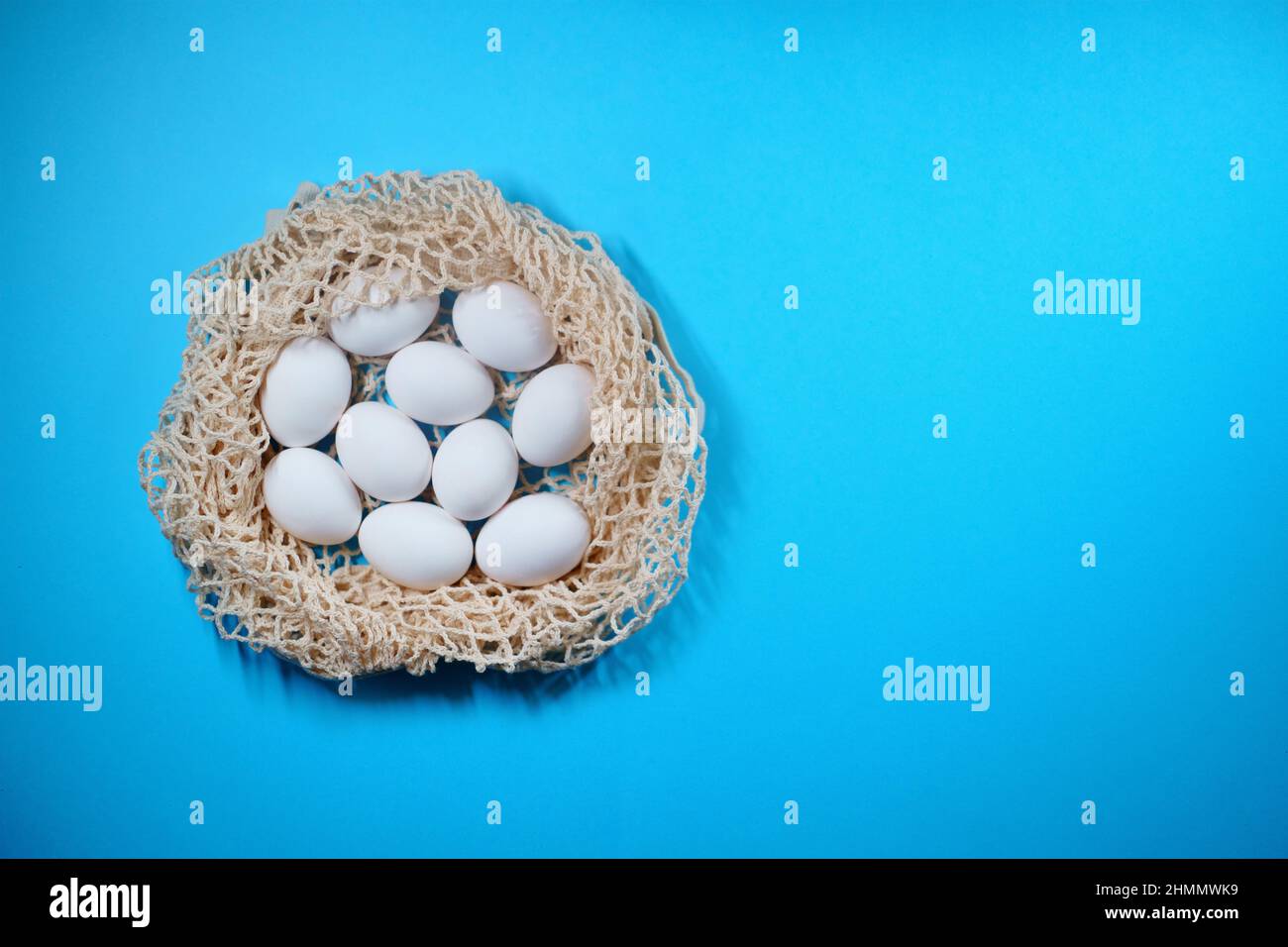 Oeufs blancs dans un sac à ficelle de nid sur fond bleu, espace de copie, Pâques, minimalisme, éco Banque D'Images