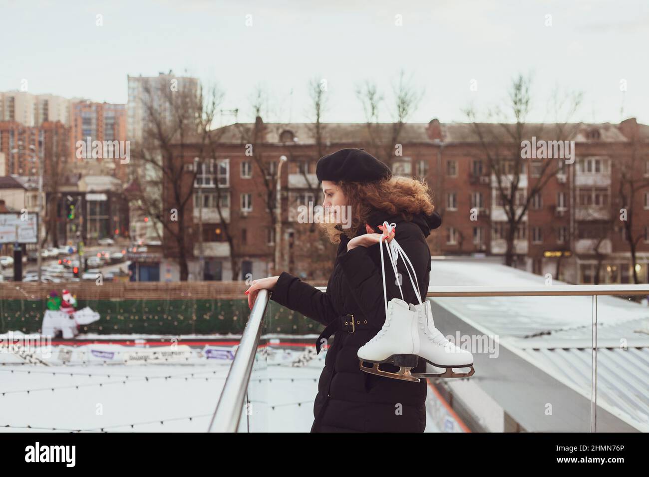 Une jeune femme à poil dur dans un béret avec des patins à glace regarde la patinoire, veut apprendre à sker Banque D'Images