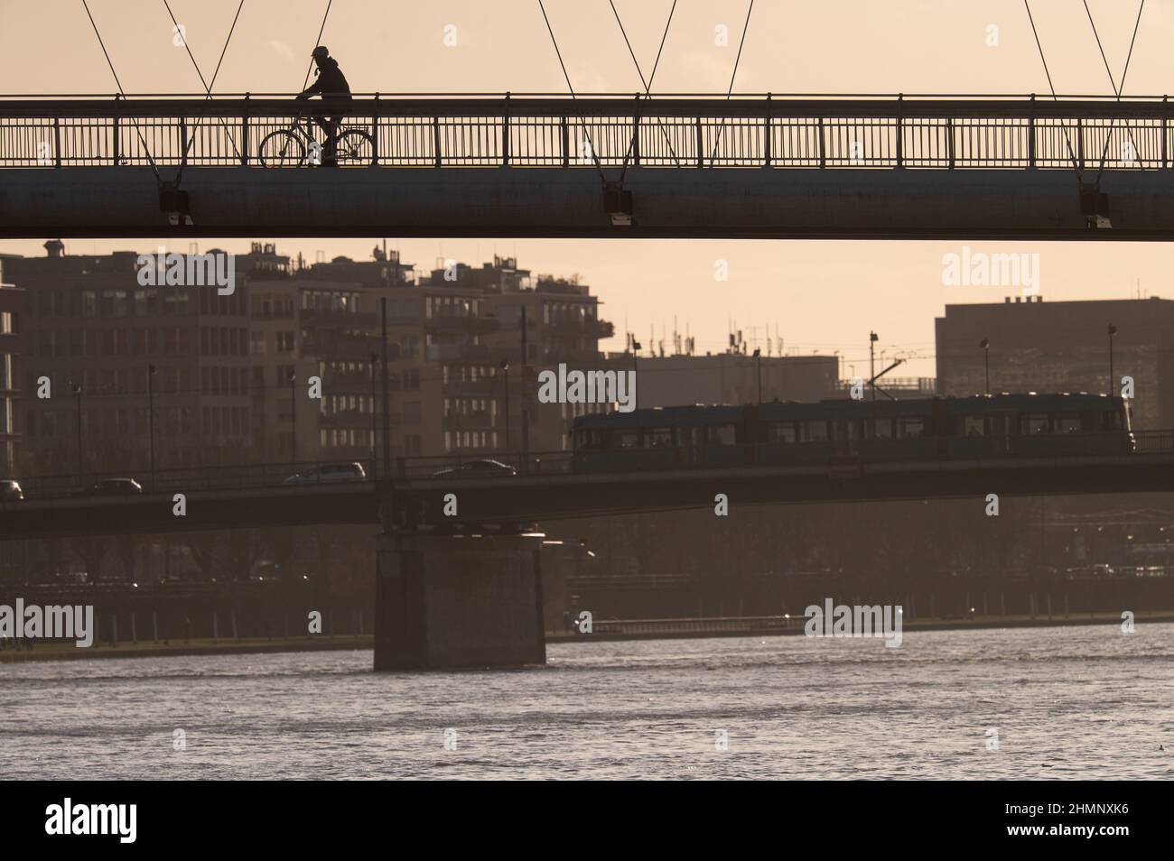 11 février 2022, Hessen, Francfort-sur-le-main : un cycliste passe au-dessus du pont Holbein. En arrière-plan, un train traverse le pont Friedensbrücke. Photo: Sebastian Gollnow/dpa Banque D'Images