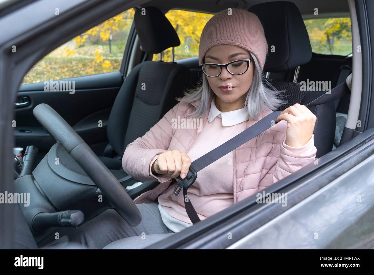 Femme asiatique à jeun une ceinture de sécurité dans la voiture avant le départ. Femme asiatique mûre prenant soin de sa sécurité. Femme asiatique blonde d'âge moyen dans la voiture. Concept de sécurité sur route. Banque D'Images