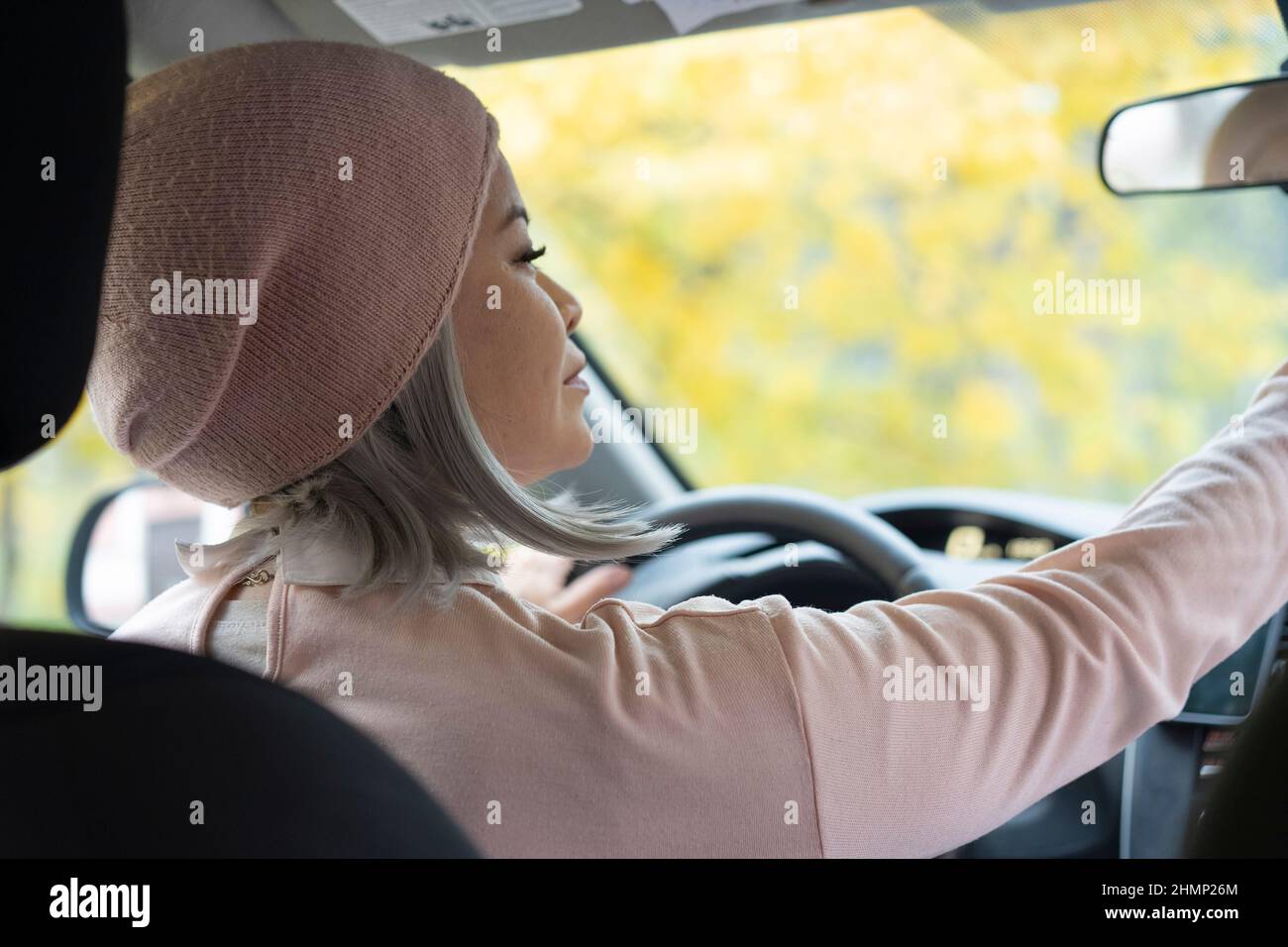 Charmante femme blonde asiatique en voiture. Femme asiatique mature en lunettes regardant le miroir tenant un volant. Femme asiatique blonde d'âge moyen dans la voiture. Femme sur la route. Concept d'entreprise. Banque D'Images
