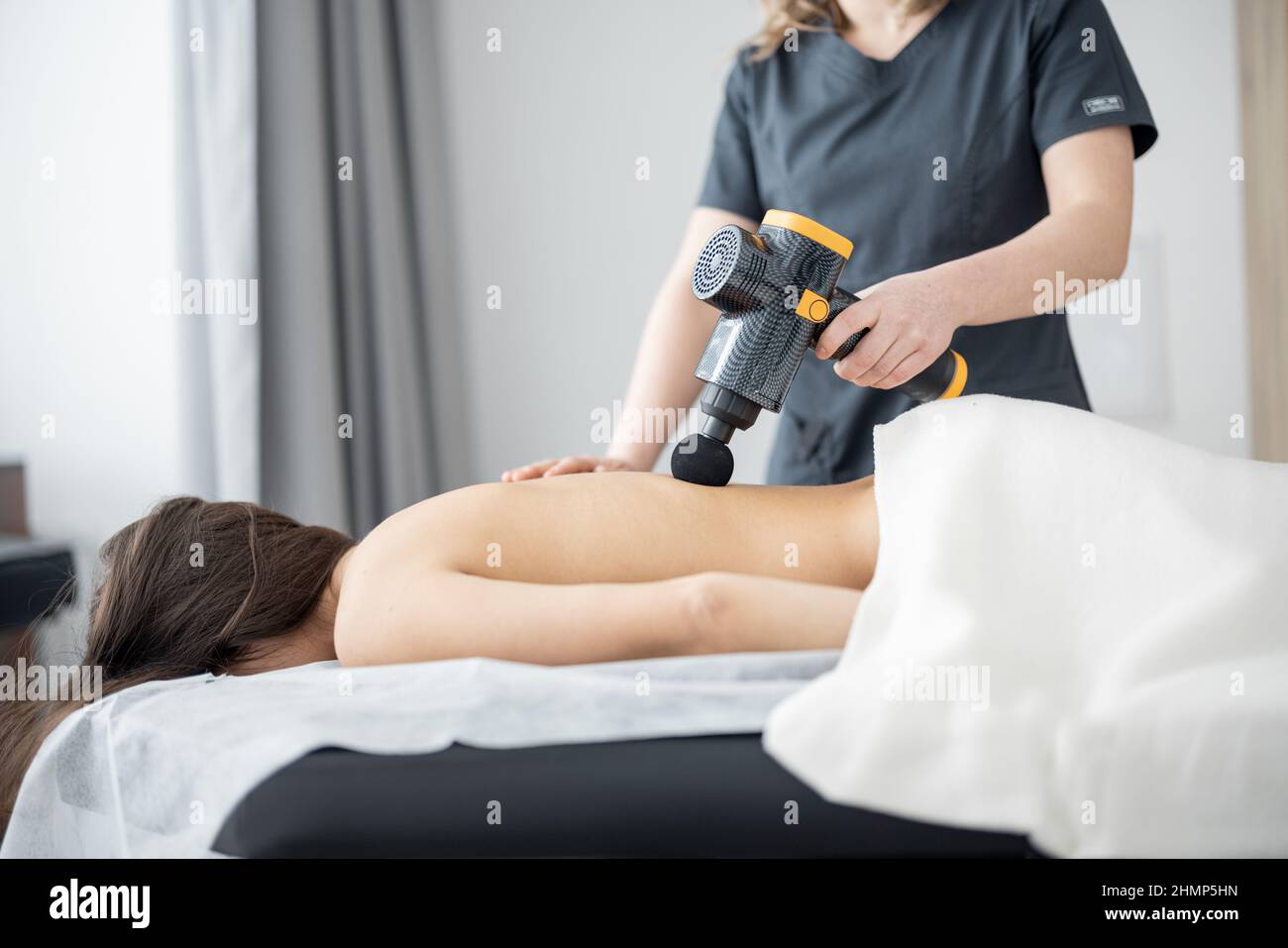 La femme fait un massage du dos du patient à l'aide d'un masseur à percussion Banque D'Images
