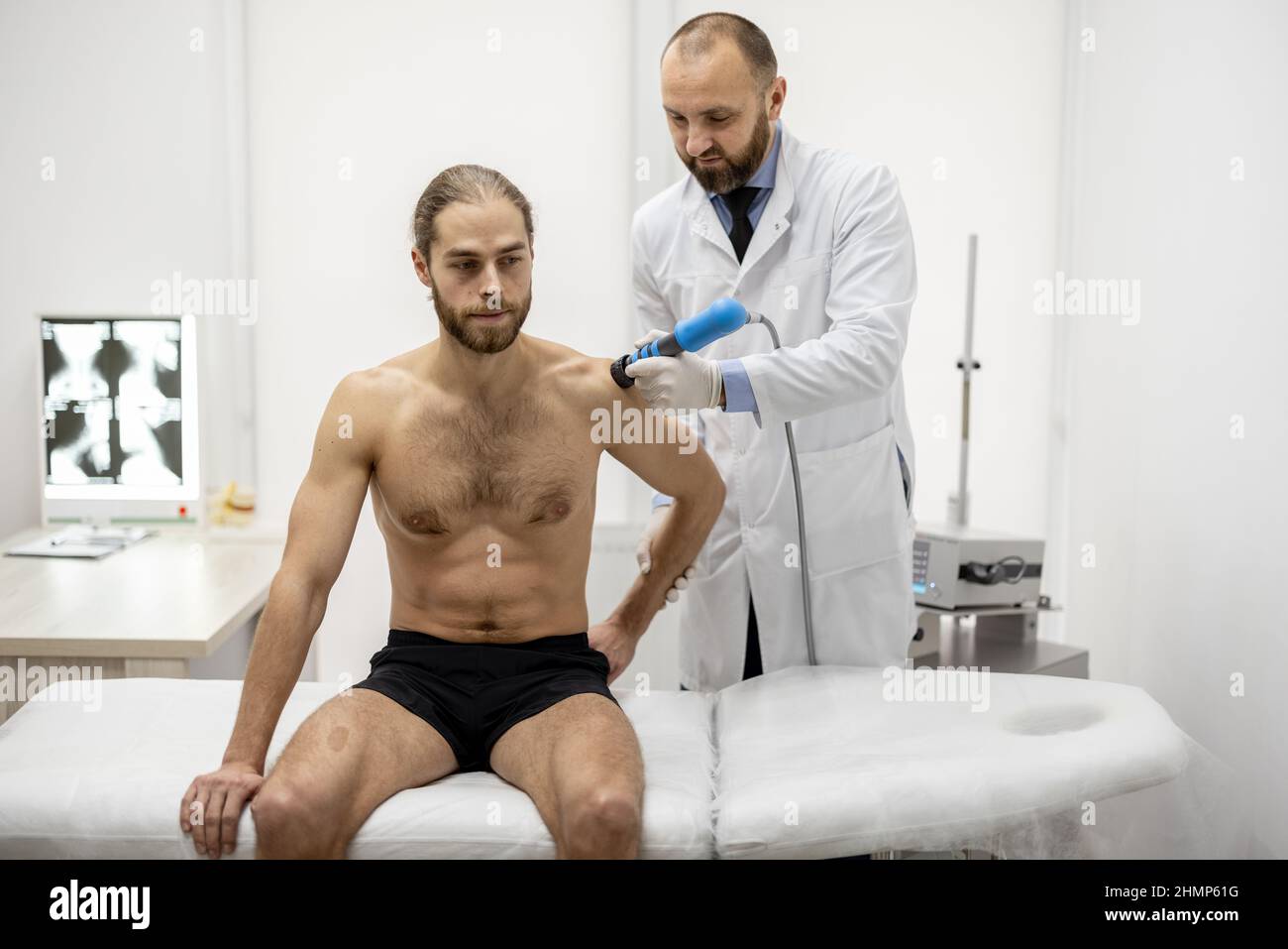 Le médecin applique un traitement par onde de choc sur l'épaule des hommes Banque D'Images