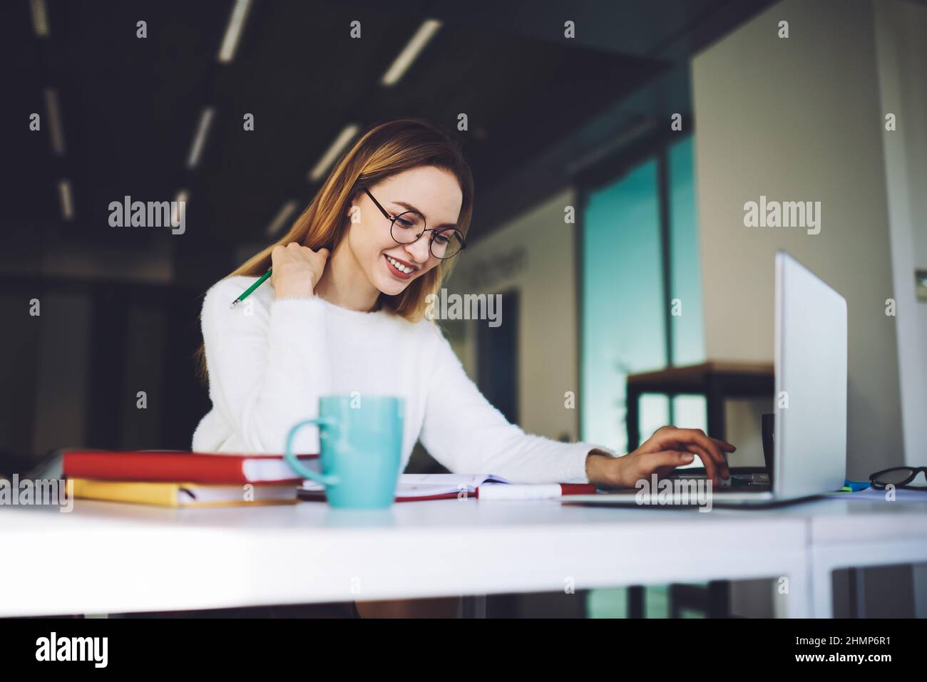 Une jeune femme heureuse qui tape sur un ordinateur portable au bureau Banque D'Images