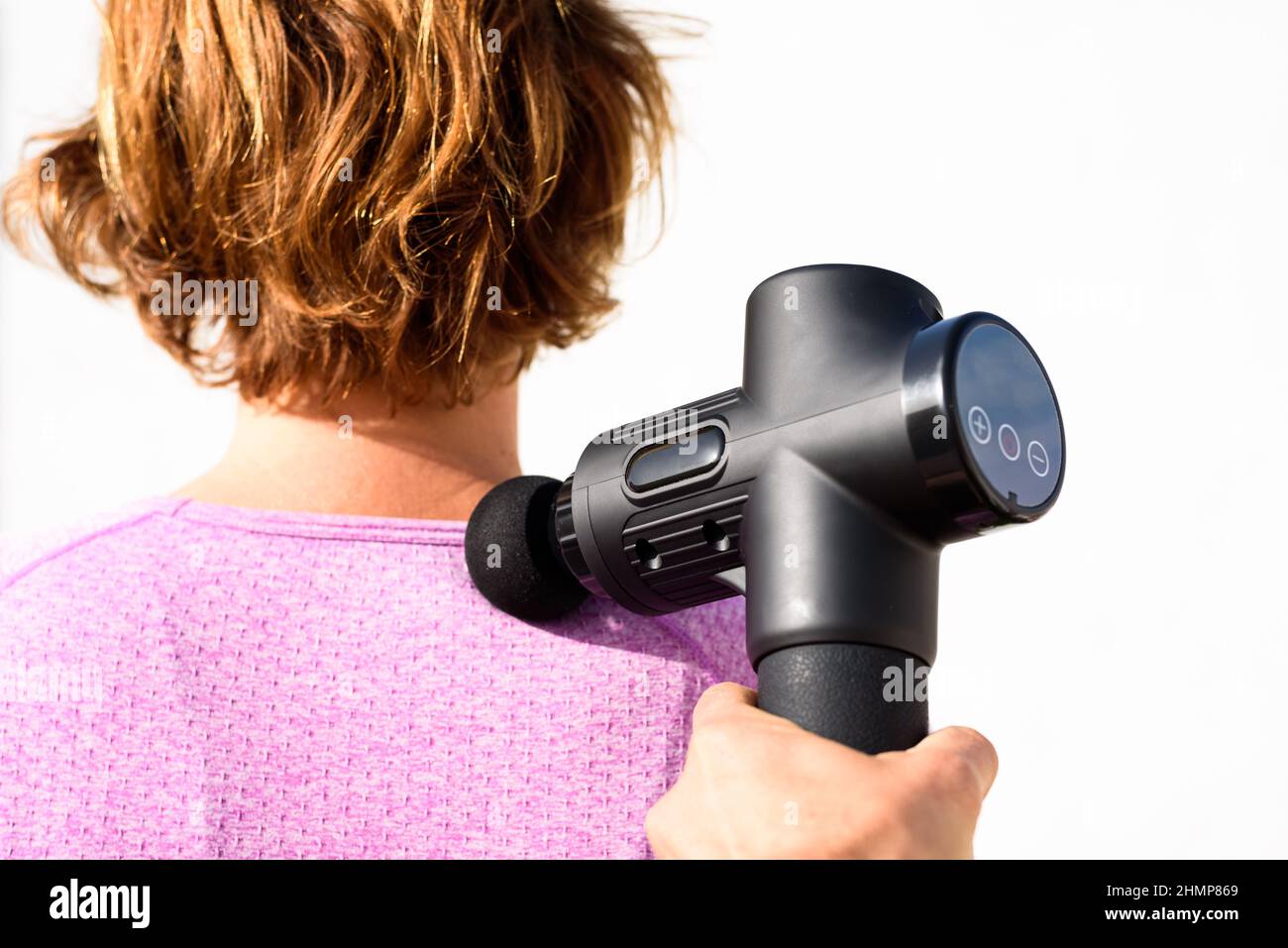Femme applique un massage avec un pistolet à percussion sur ses épaules, isolé sur fond blanc. Banque D'Images