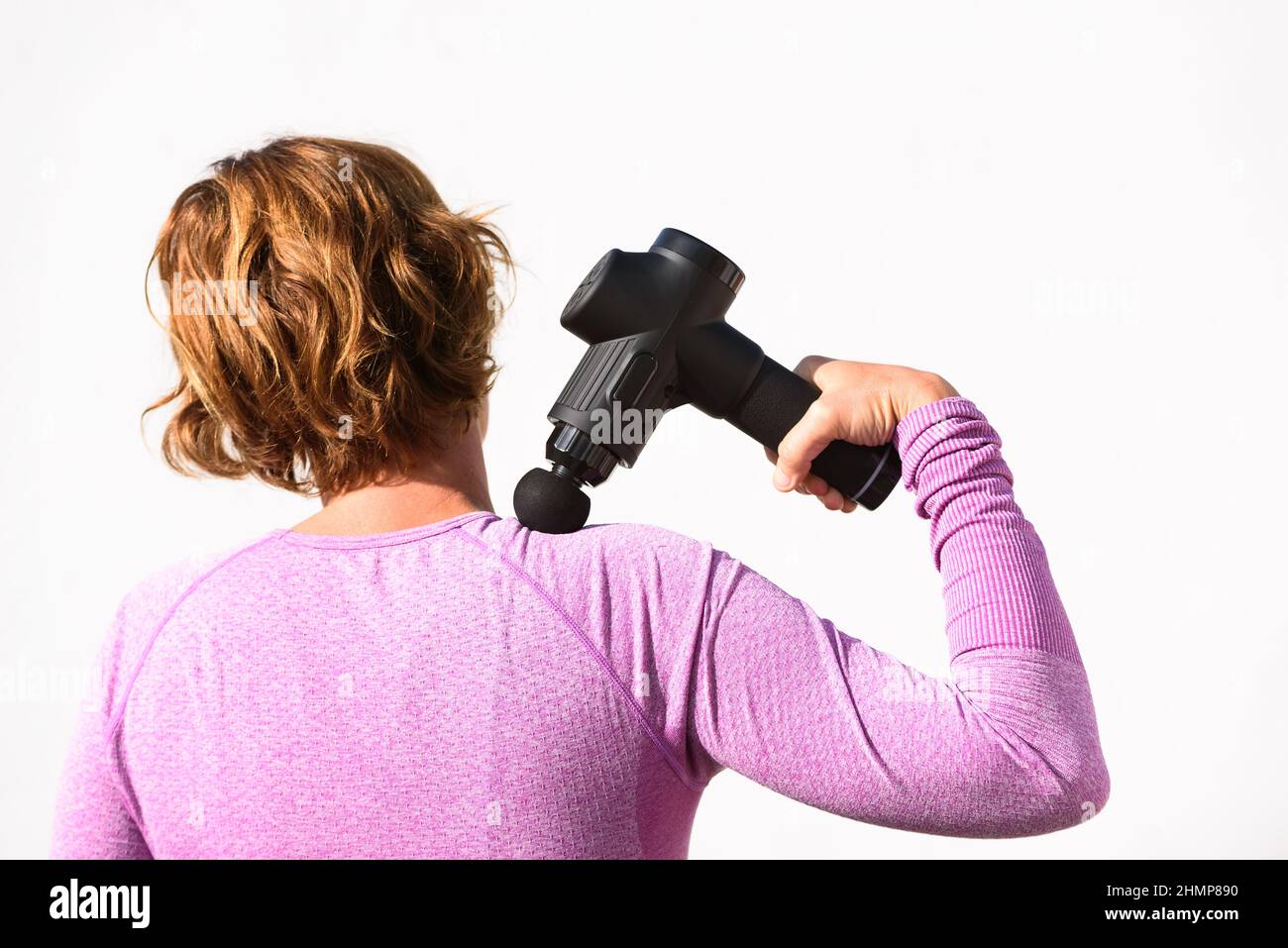 Femme applique un massage avec un pistolet à percussion sur ses épaules, isolé sur fond blanc. Banque D'Images
