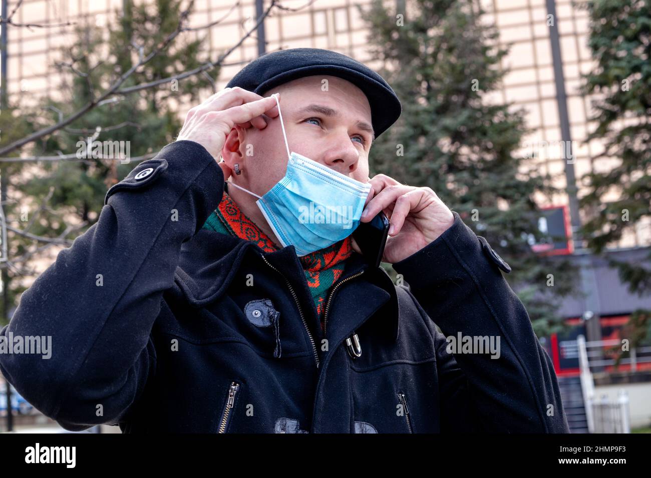 Jeune homme qui prend son masque pour faire un appel téléphonique. À l'extérieur. Mesures de protection contre le coronavirus. Banque D'Images