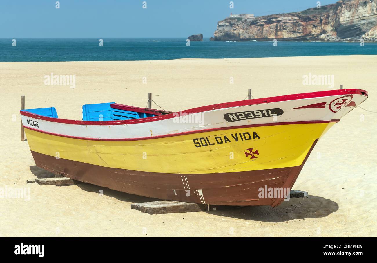 Nazaré, Portugal - avril 2018: Vieux bateau de pêche traditionnel coloré en bois sur la plage du village de pêcheurs de Nazaré. La haute falaise de Nazaré Sitio Banque D'Images