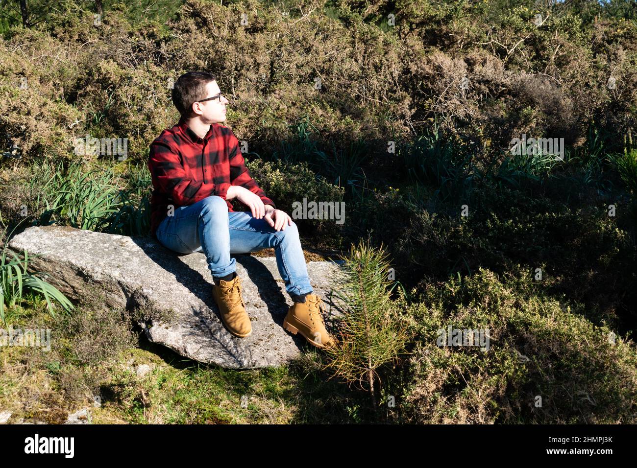 Homme dans un maillot de bûcherons assis sur un rocher dans la forêt, Espagne Banque D'Images