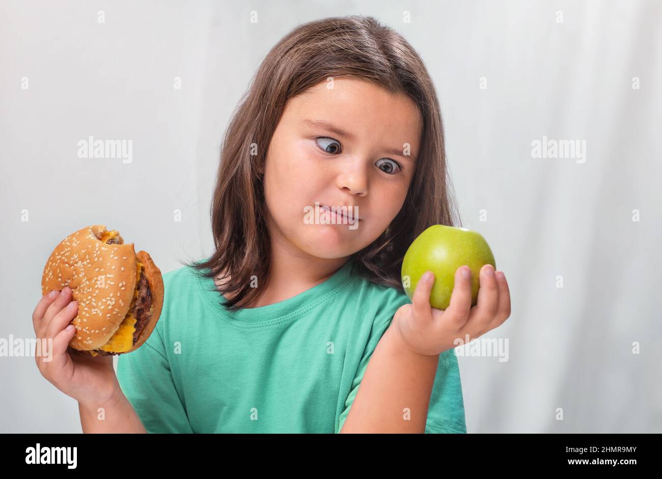 Un enfant regarde une pomme par surprise après avoir piquer dans un hamburger Banque D'Images