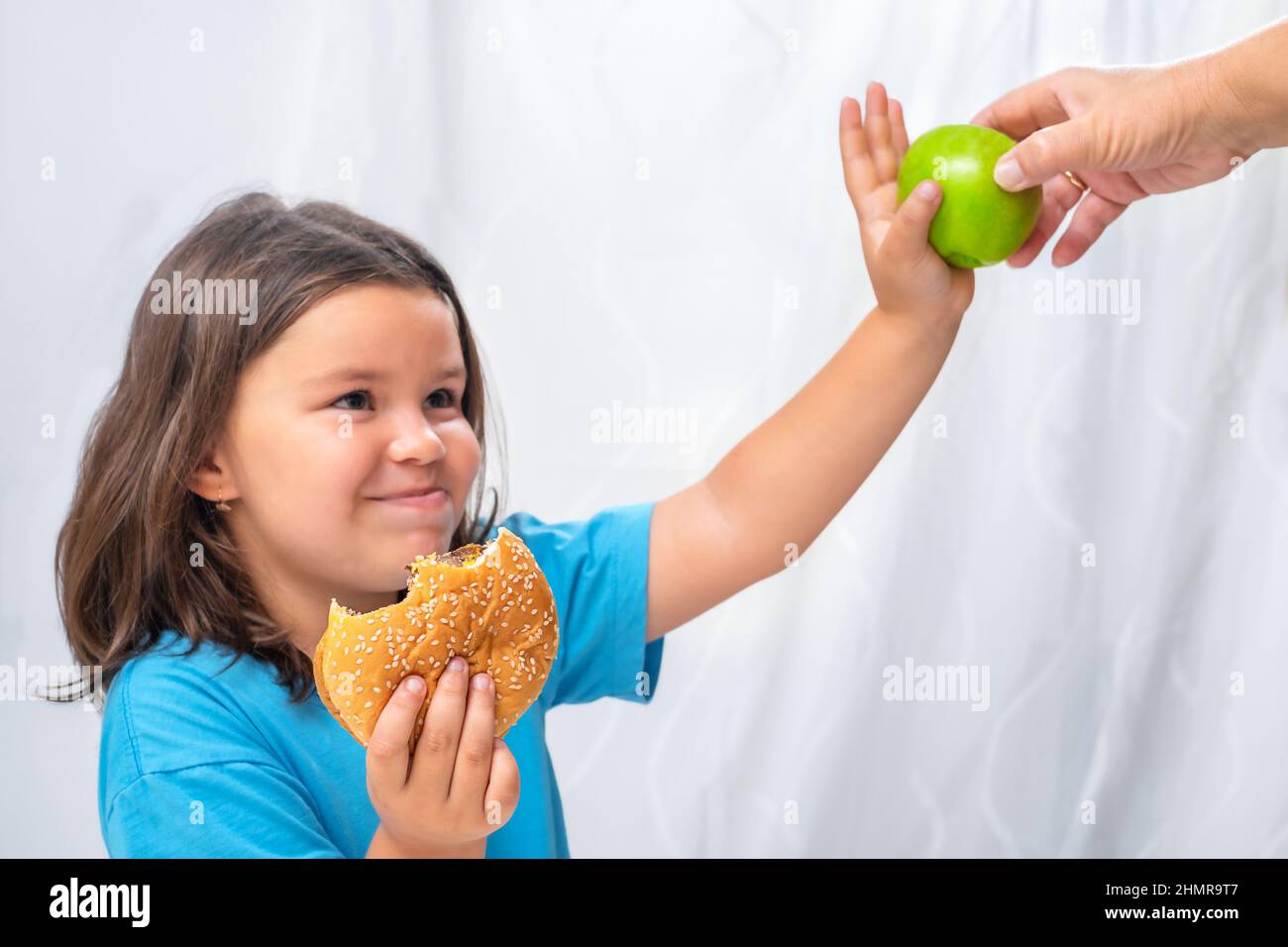 L'enfant refuse une pomme des mains d'un aîné et choisit un hamburger Banque D'Images