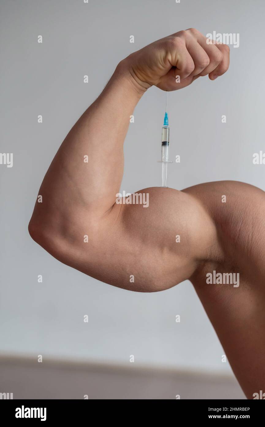 Gros plan des biceps mâles. Le bodybuilder masculin méconnaissable se met une injection de testostérone. L'athlète sans visage prend l'hormone de croissance. Verticale . Banque D'Images