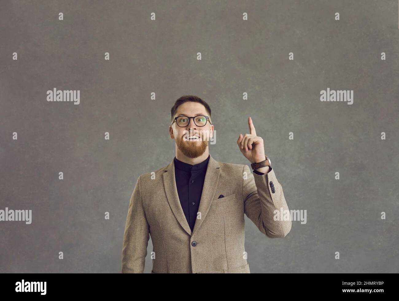 Portrait d'homme d'affaires heureux en costume et lunettes pointant le doigt vers le haut frappé par une grande idée Banque D'Images
