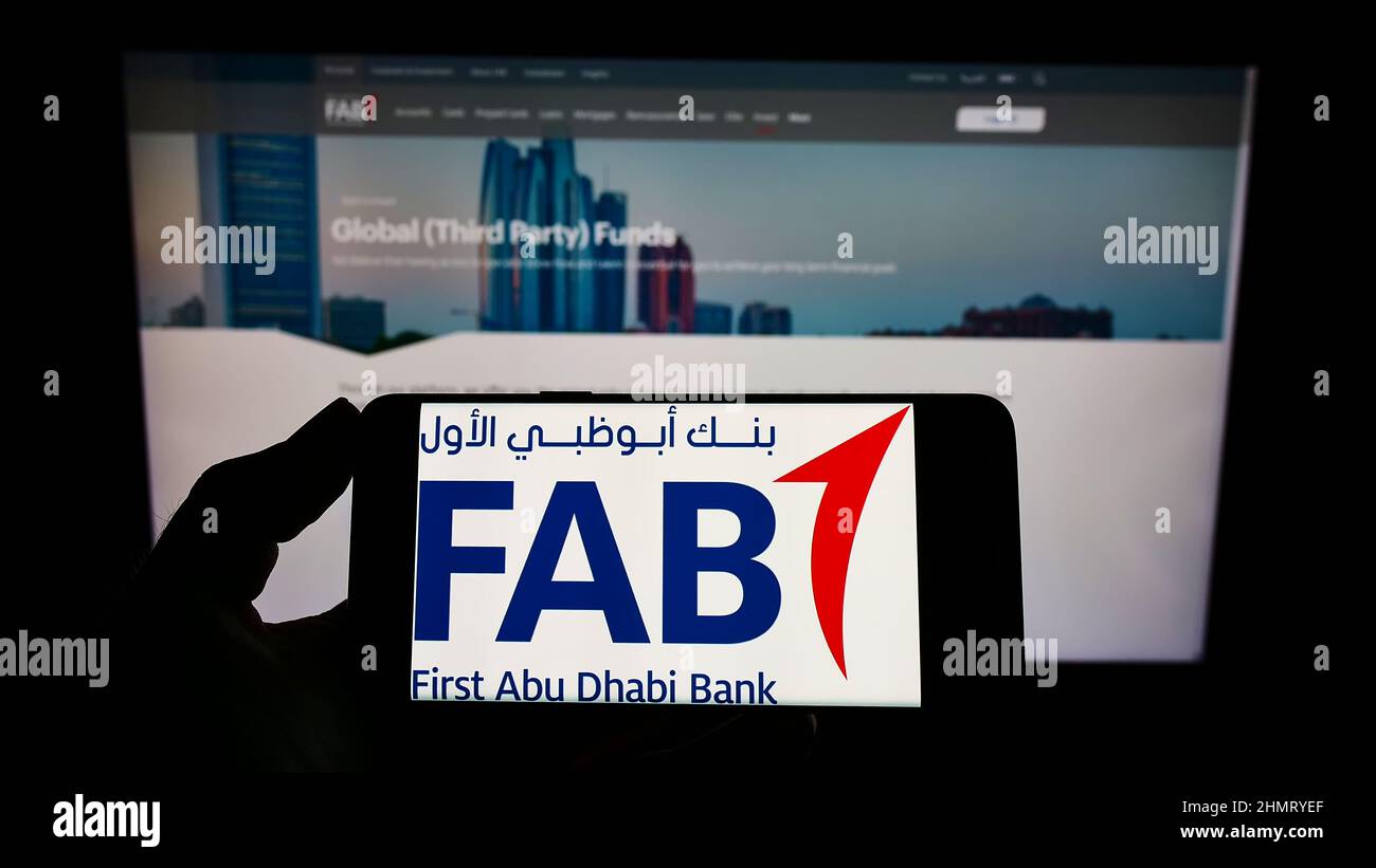Personne tenant un téléphone portable avec le logo de la société financière First Abu Dhabi Bank (FAB) à l'écran en face de la page Web. Mise au point sur l'affichage du téléphone. Banque D'Images