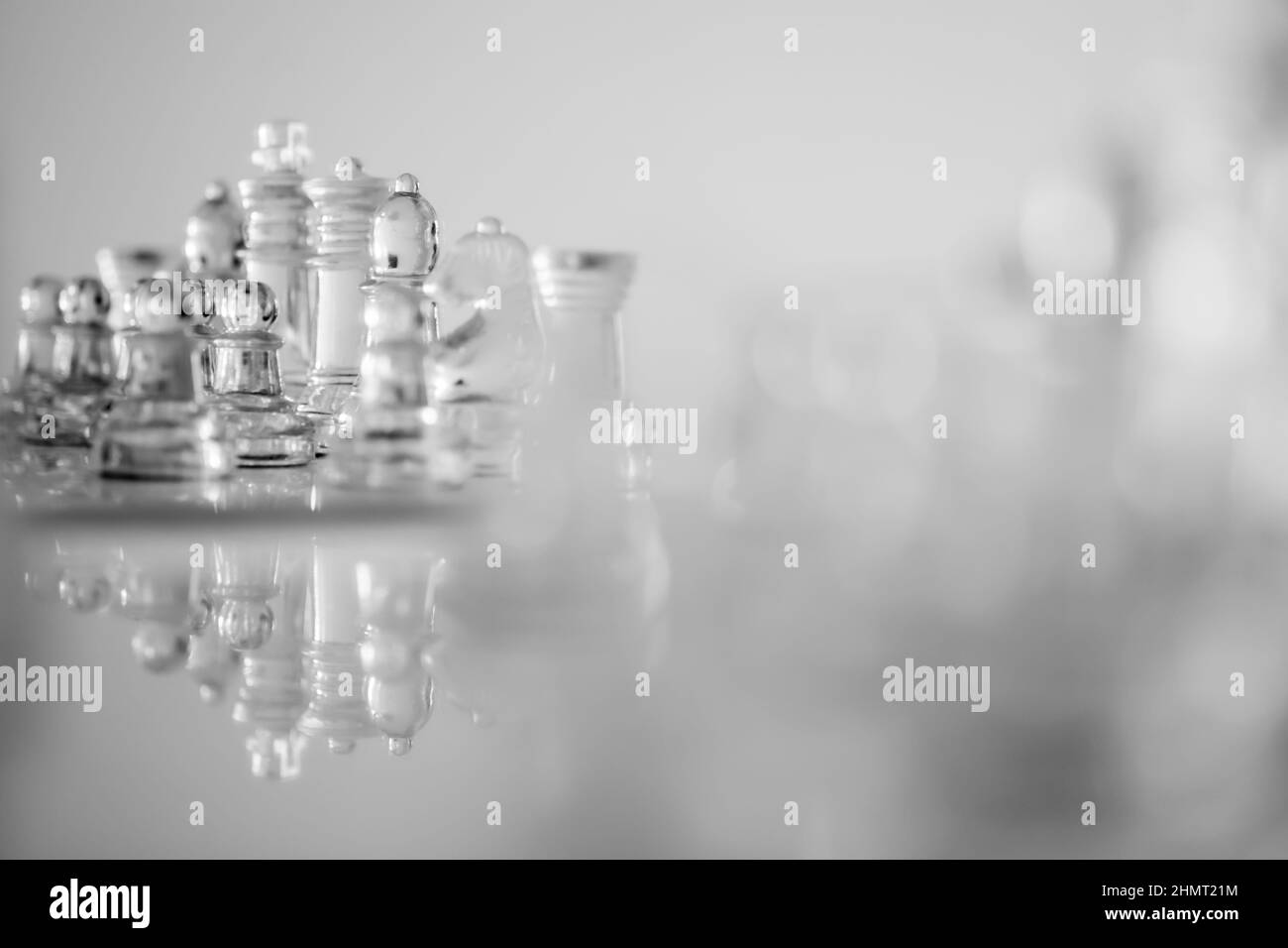 Ensemble réfléchi de pièces d'échecs en verre flou de premier plan avec la reine et le roi focalisé. Les échelles de gris s'affichent sur fond blanc. Banque D'Images