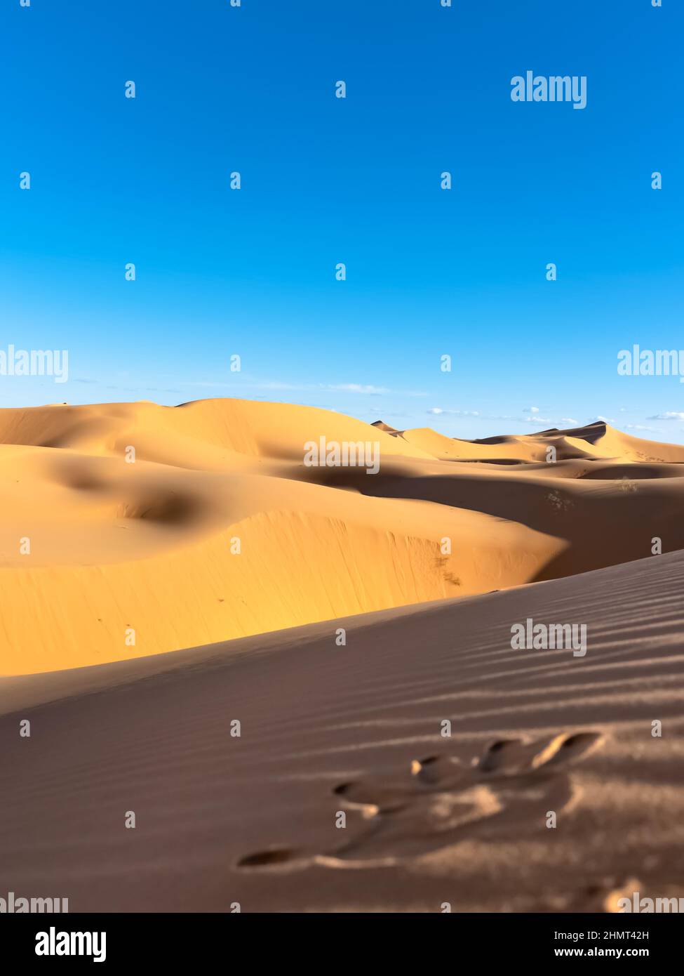 Imprimé à la main dans le sable au premier plan avec dunes de sable jaune de couleur dorée et ciel bleu nuageux en arrière-plan. Banque D'Images