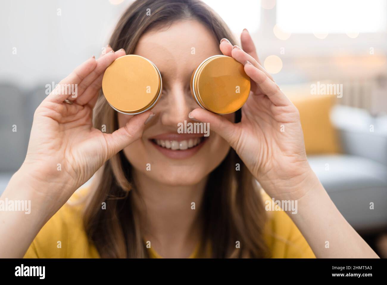 Jeune femme tenant de la crème cosmétique dans un contenant en métal dans ses mains, cachant ses yeux Banque D'Images