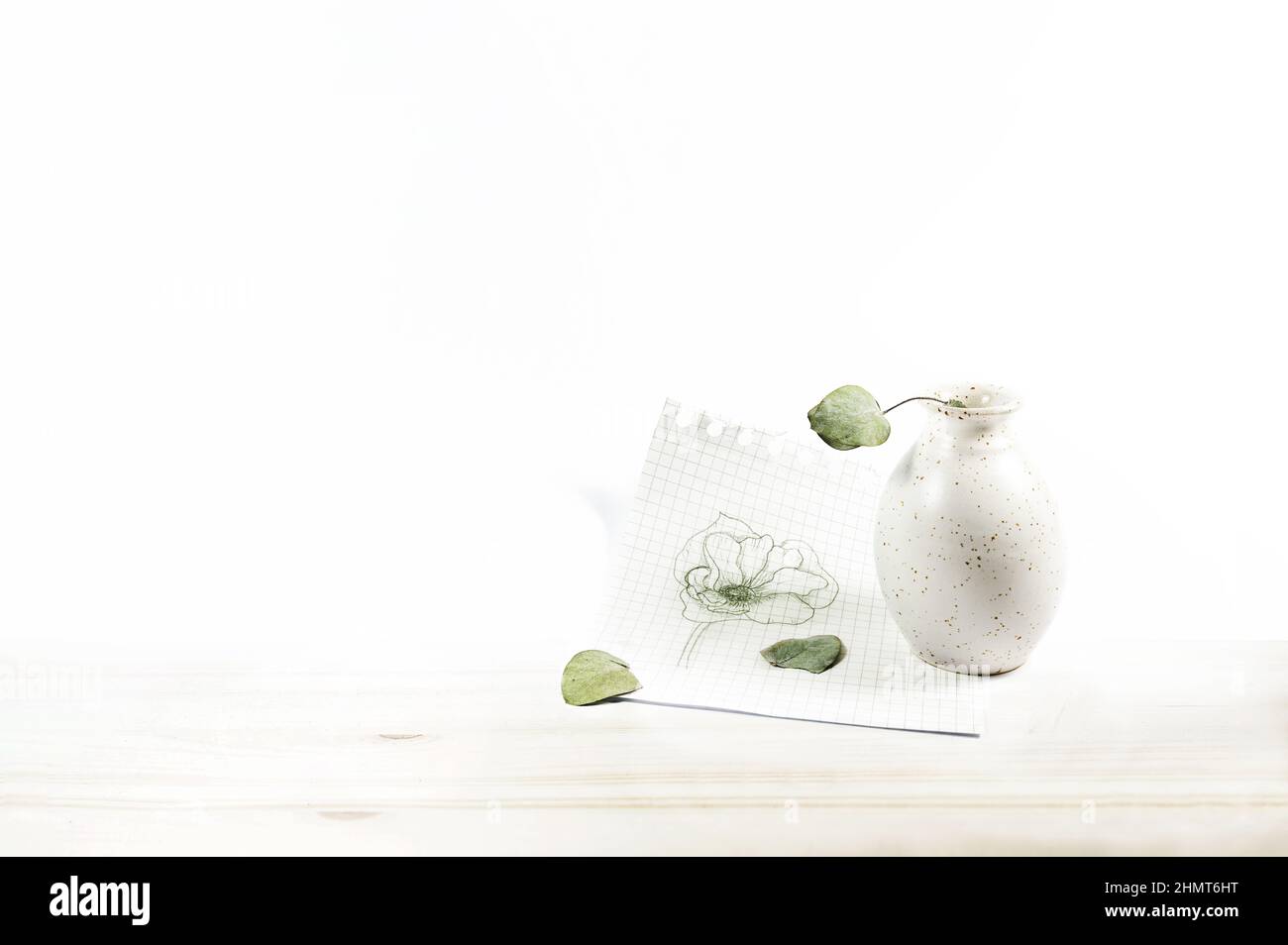 Petit vase vide avec des feuilles sèches et une fleur dessinée sur une feuille de papier quadrillé sur une table en bois brillant contre le mur blanc, généreux Copy spa Banque D'Images