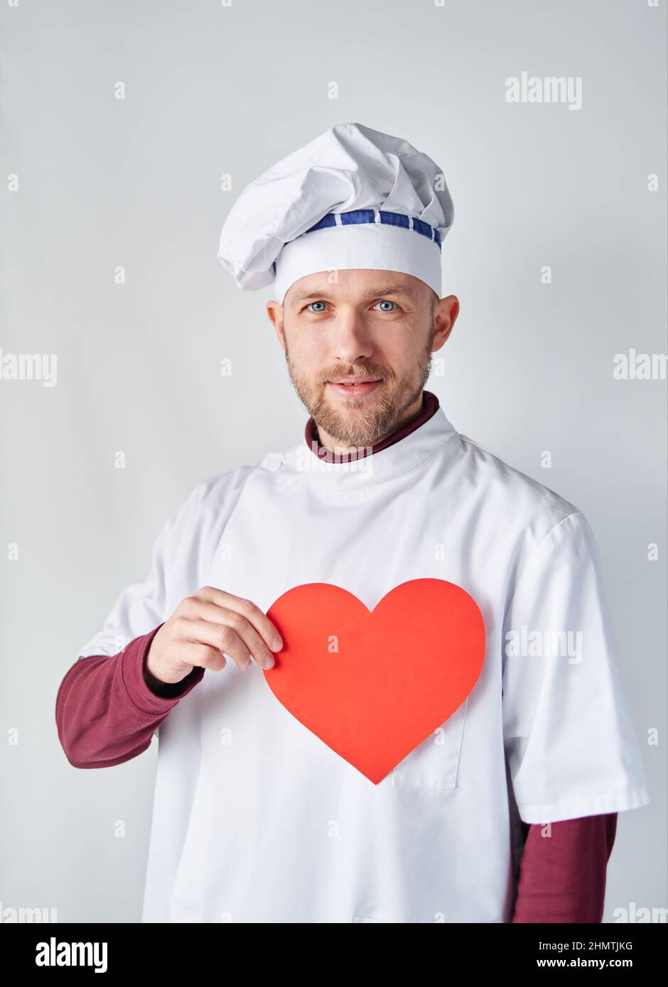 Boulanger ou chef à barbe en uniforme blanc avec coeur en papier rouge.  Restaurant de concept de café. Chef cuisinier tenant un coeur rouge devant  le vêtement de travail. Photo de haute