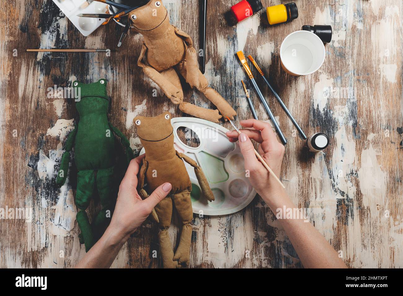 Grenouille poupée douce à la main.Bricolage fabrication de cadeaux.Les mains humaines tiennent le jouet mou grenouille.Accessoires pour travaux d'aiguille sur fond gris.Décoration maison faite à la main.Processus de Banque D'Images